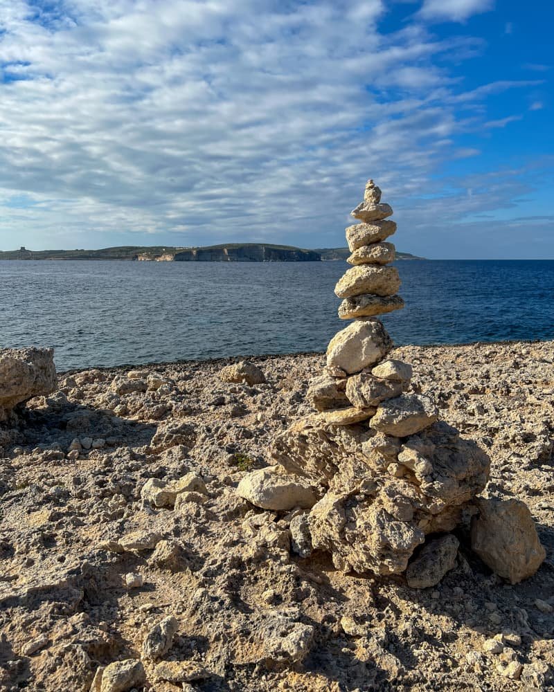 Sara Claeys die uitkijkt over een rotsachtige klif in Mellieha, Malta, als symbool voor het vinden van rust en een nieuw perspectief na de 'hustle'-cultuur.