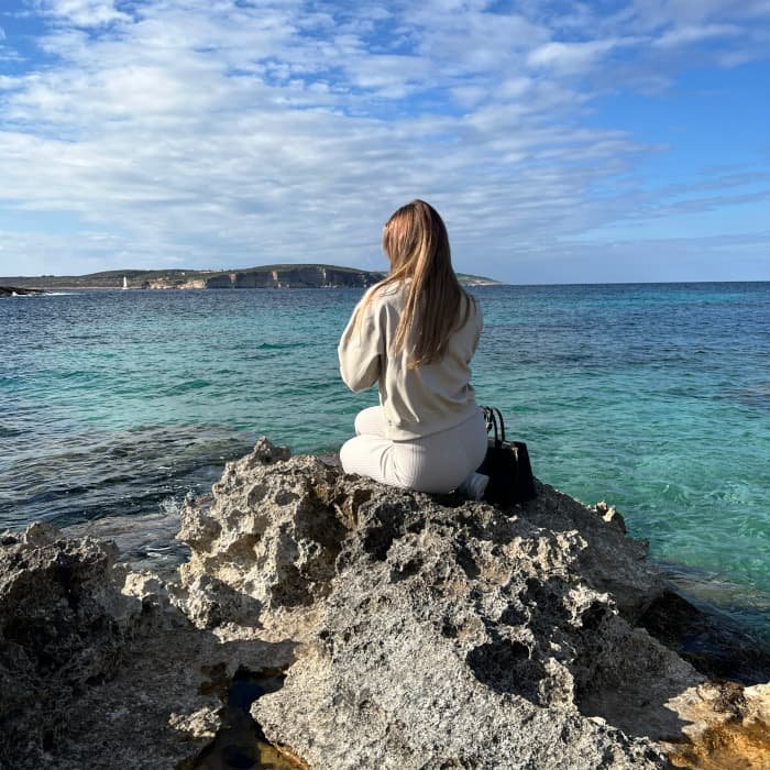 Sara Claeys, oprichter van Adverdream, zittend op een rots in Mellieħa, Malta, als symbool voor de rust en inspiratie die haar gronden.