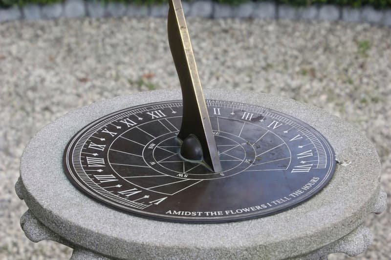 Een stenen zonnewijzer in een serene tuin, symbool voor de heldere, strategische richting die Adverdream biedt aan ondernemers.