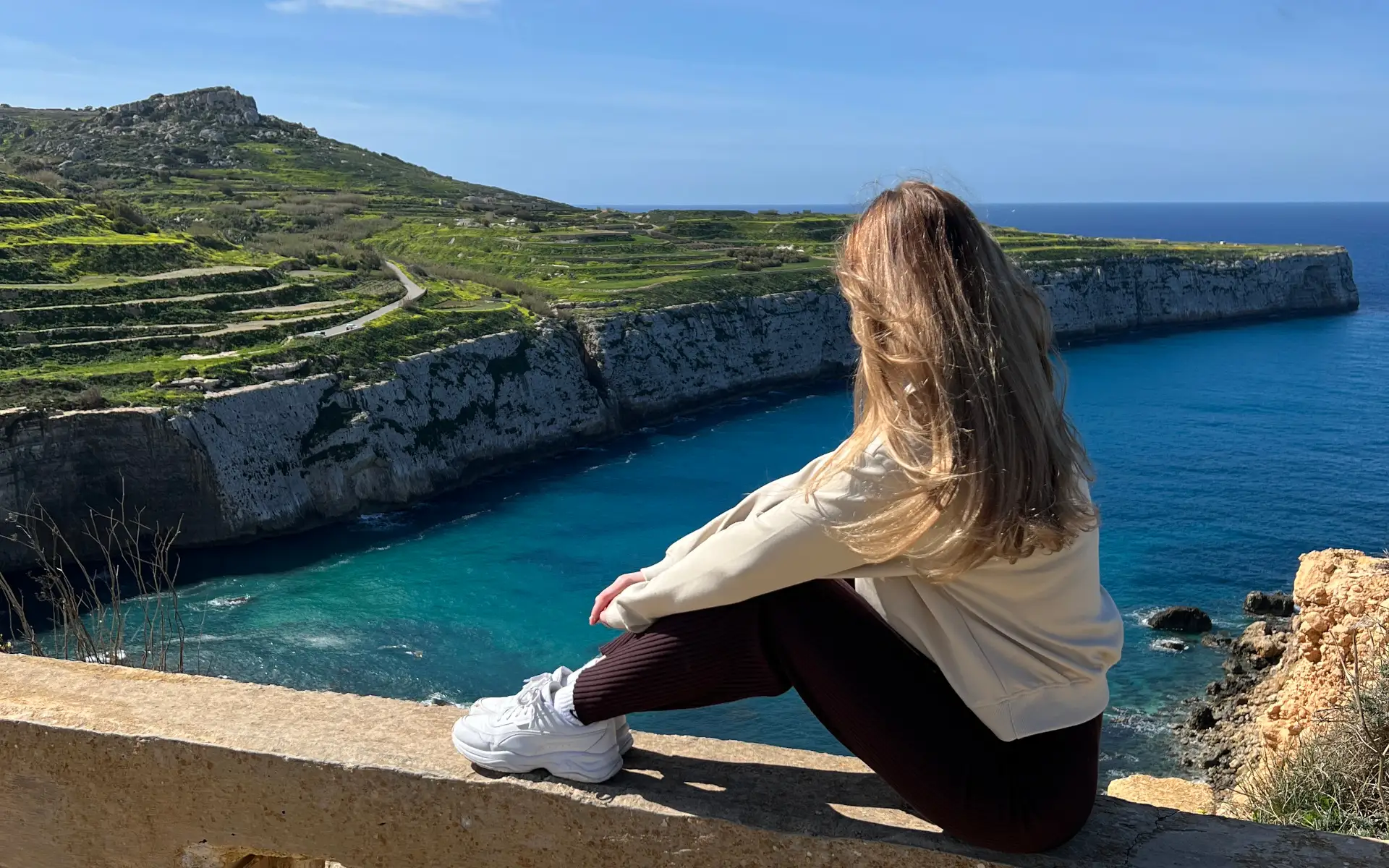 Sara Claeys die uitkijkt over een rotsachtige klif in Mellieha, Malta, als symbool voor het vinden van rust en een nieuw perspectief na de 'hustle'-cultuur.